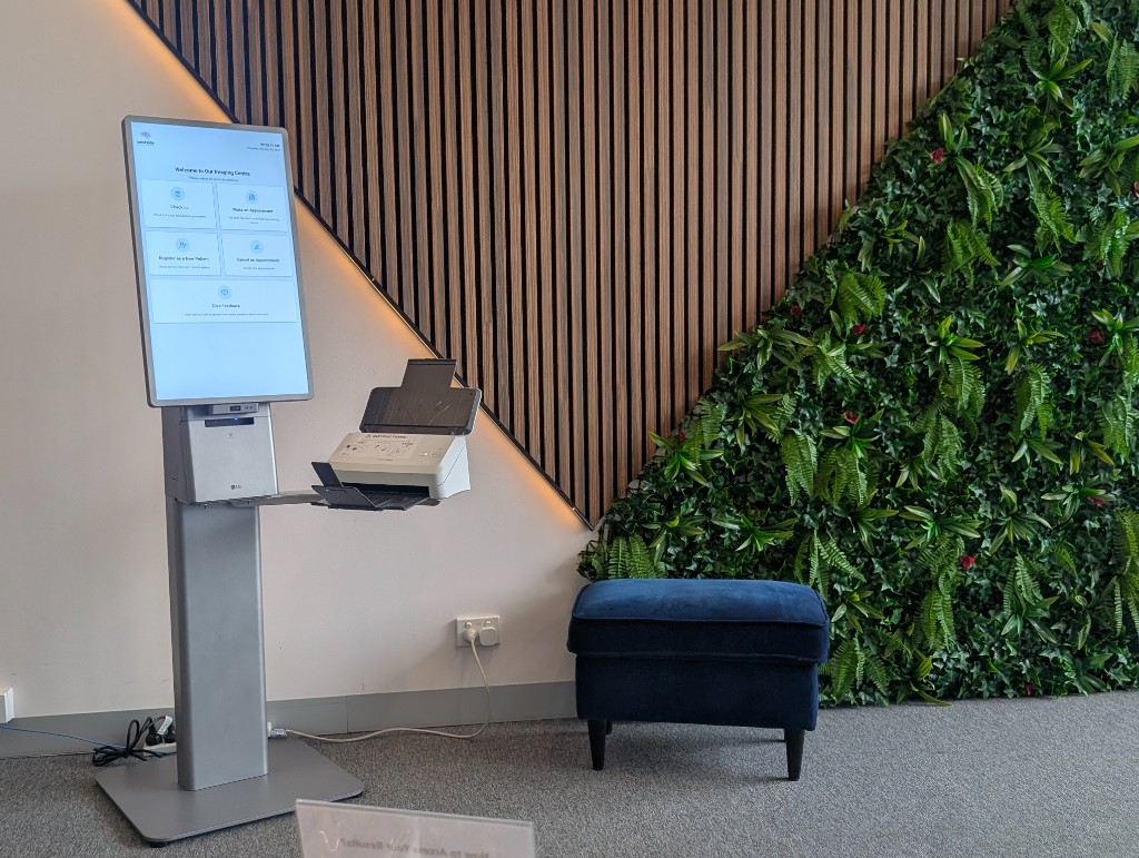 Self-service imaging clinic kiosk with vertical touchscreen showing welcome options and side-mounted document scanner