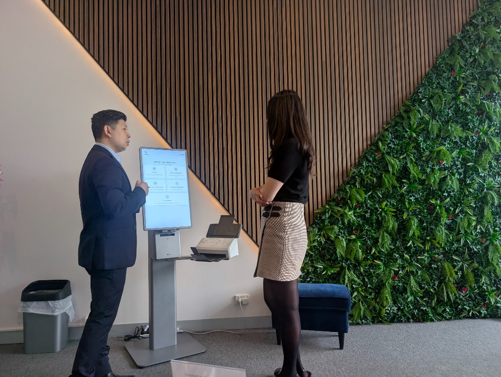 Photo of kiosk welcome screen with four large action tiles and staff nearby