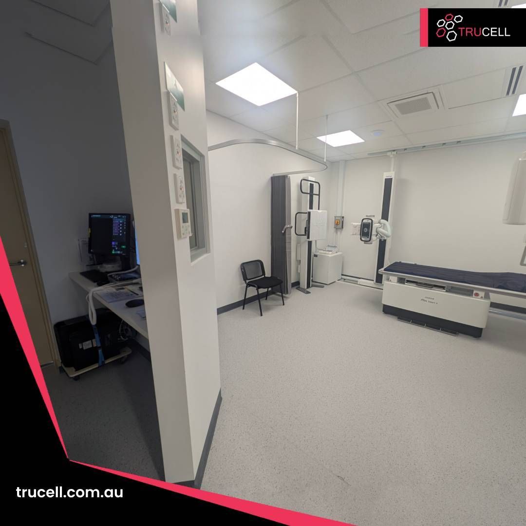 Care Plus Imaging Doncaster X-ray room: Fujifilm flat-panel detector unit, clinical workstation with multi-channel patient monitor, and the radiographer control area visible through the leaded window